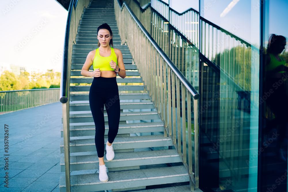 Young caucasian female 20s jogging outdoors training cardio and athletic strength outdoors, attractive slim sports woman with perfect body shape running down on stairs motivated with fitness goals