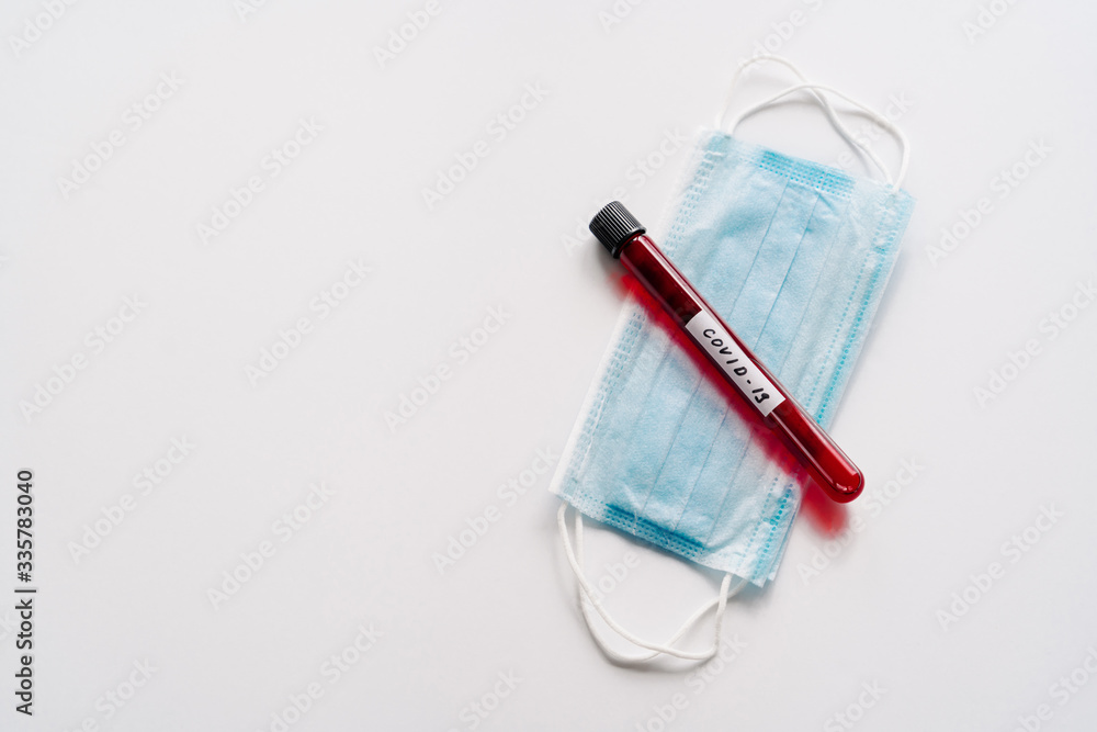 Test tube containing blood samples for coronavirus testing or analyzing, sterile medical mask on white background. Chemical analysis in laboratory. Biohazard protection Test tube containing blood samples for coronavirus testing or analyzing, sterile medical mask on white background. Chemical analysis in laboratory. Biohazard protection
