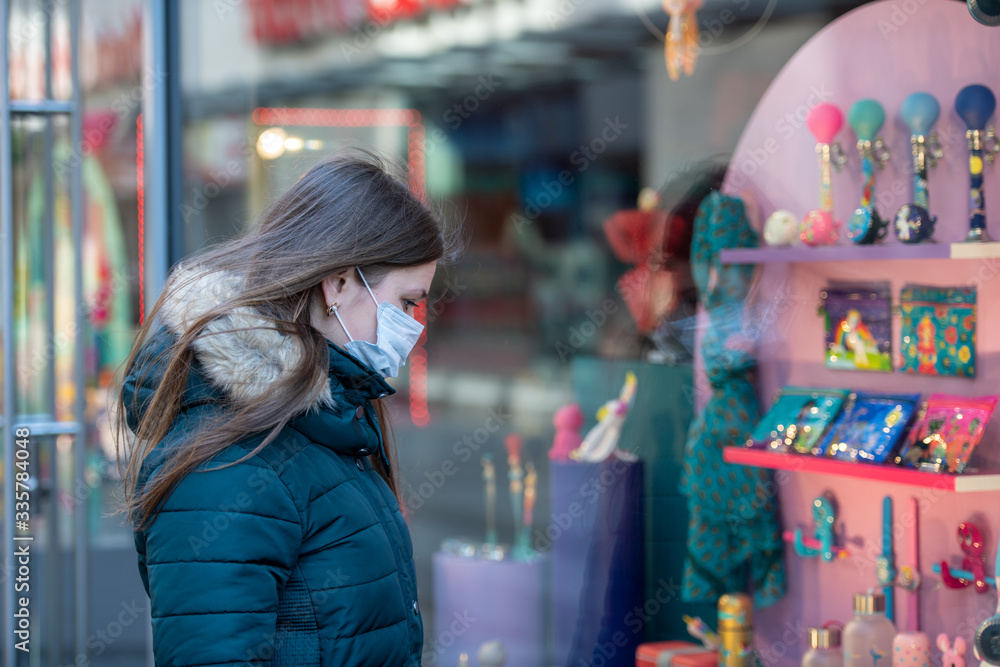 Young woman wearing medical protective mask in the front of clodes shop