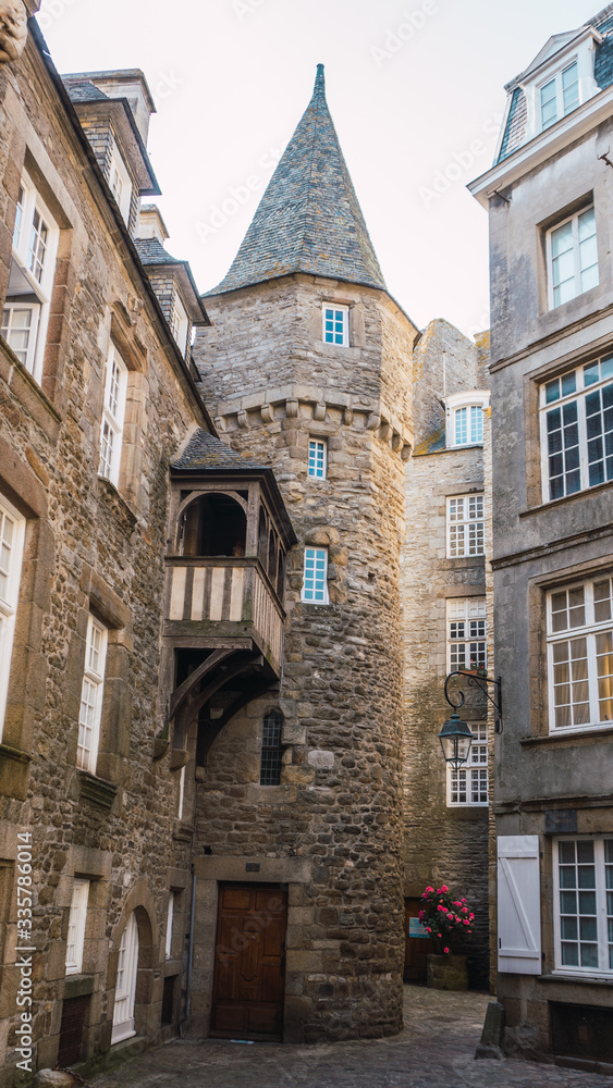 Old stone tower in Saint Malo in French Brittany, stone construction with half-timbered balcony and white windows with old street lighting.