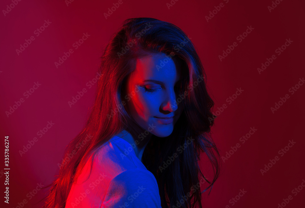Portrait of young woman with blue and red trendy colored light. Neon Studio shot. Back lit moody attractive brunette female on dark background. Melancholy, thoughtful beauty concept. Romantic mood