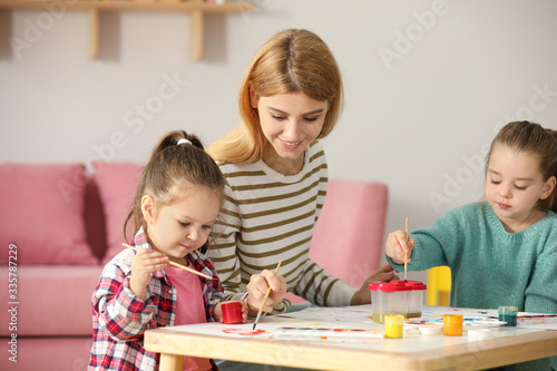 Mother and daughters painting at table indoors. Playing with children