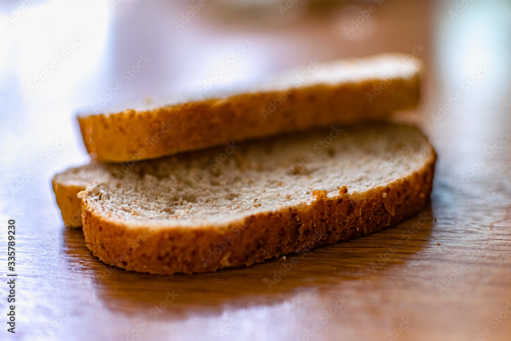 Two sliced slices of bran bread with a crisp crust of rye flour, lying on a brown wooden table, after fresh baking in the kitchen in the sunlight