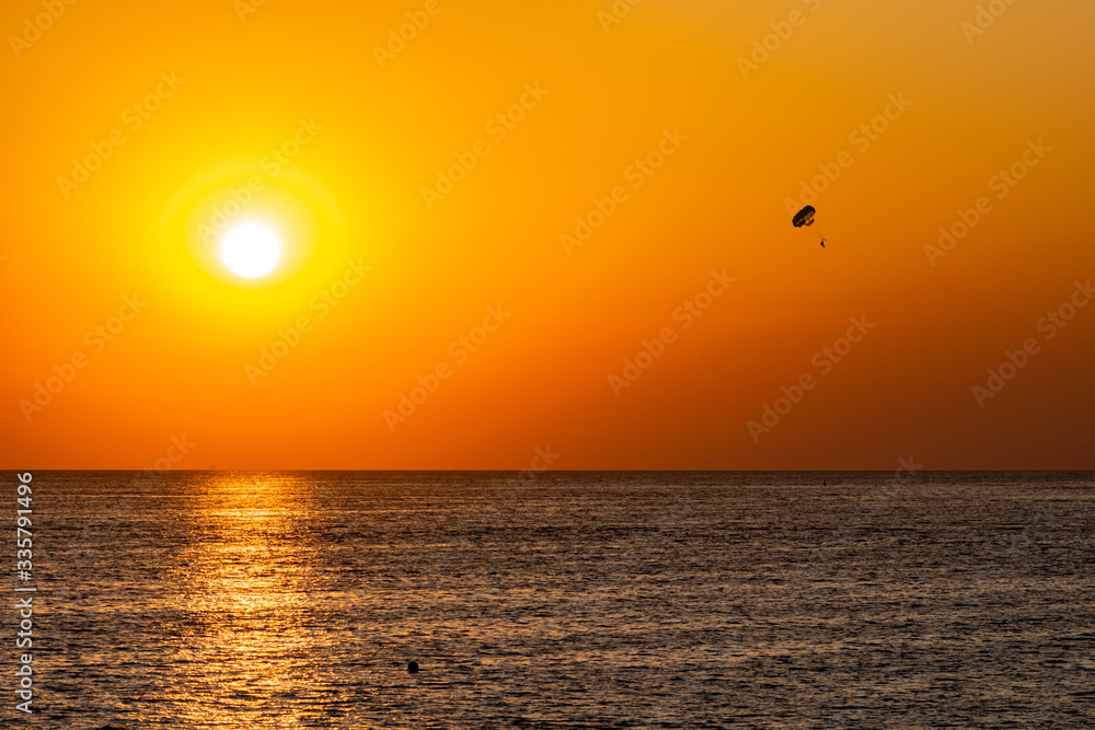 Silhouette of a parachute and a skydiver against the background of a bright burning sunset over the sea. A shining sun and an object flying in the yellow sky. Silhouette of a parachute and a skydiver against the background of a bright burning sunset over the sea. A shining sun and an object flying in the yellow sky.