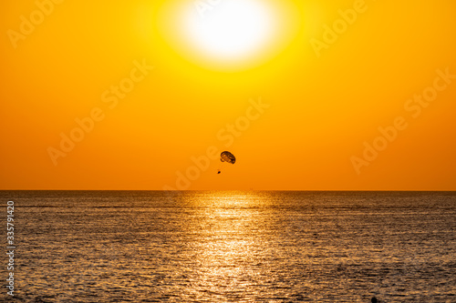 Silhouette of a parachute and a skydiver against the background of a bright burning sunset over the sea. A shining sun and an object flying in the yellow sky.