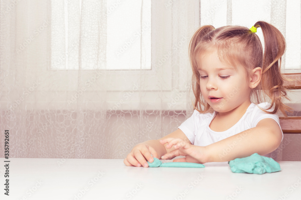 girl preschooler sits at a table and sculpts from turquoise dough for modeling. activities with children at home on self-isolation in connection with coronavirus infection girl preschooler sits at a table and sculpts from turquoise dough for modeling. activities with children at home on self-isolation in connection with coronavirus infection