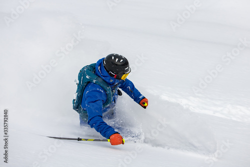 Freeride skier rides over off-piste slope in snow capped forest. Skier enjoying a deep powder turn.