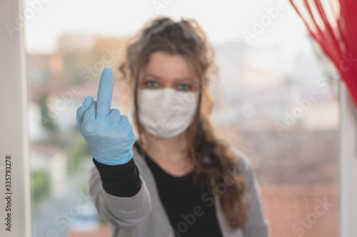 young woman wearing surgical mask and gloves is making obscene gesture 