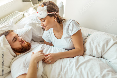 cute young caucasian woman look at sleeping man with love. married couple on bed in the morning. weekend, holiday, morning at home