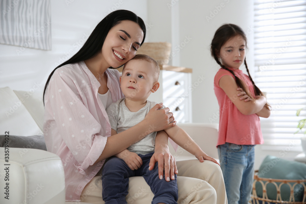 Unhappy little girl feeling jealous while mother spending time with her baby brother at home Unhappy little girl feeling jealous while mother spending time with her baby brother at home
