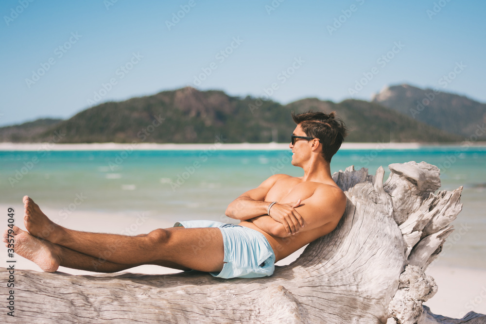 Male model wearing sunglasses and fitness body on the beach posing