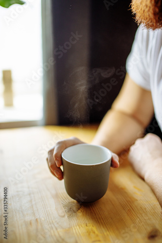 close-up photo of a cup of hot tea, steam from the mug rises. unrecognizable male hold a cup going to drink it. morning