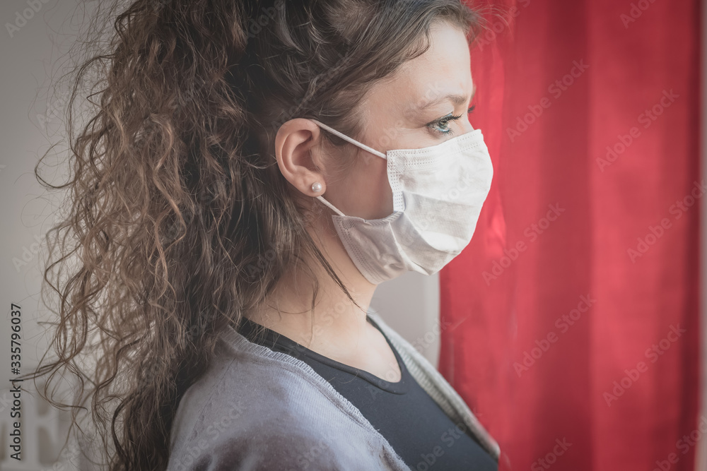 young woman wearing a surgical mask looking through the window