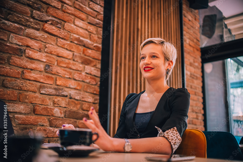 Image of a young attractive businesswoman with a cup of coffee working with her clients in a cafe bar.. Image of a young attractive businesswoman with a cup of coffee working with her clients in a cafe bar..