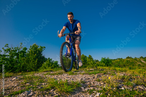 Adventurous Cyclist riding his mountain bike at the edge of a cliff, on rocky terrain while wearing no safety equipment.Amazing top view.