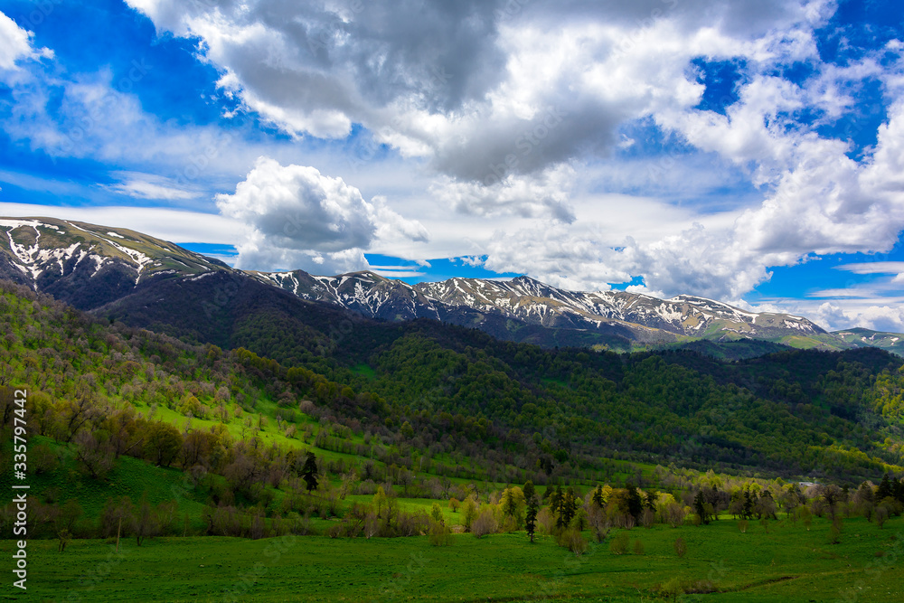 Beautiful mountain panorama with lush greens, blue skies, and puffy clouds