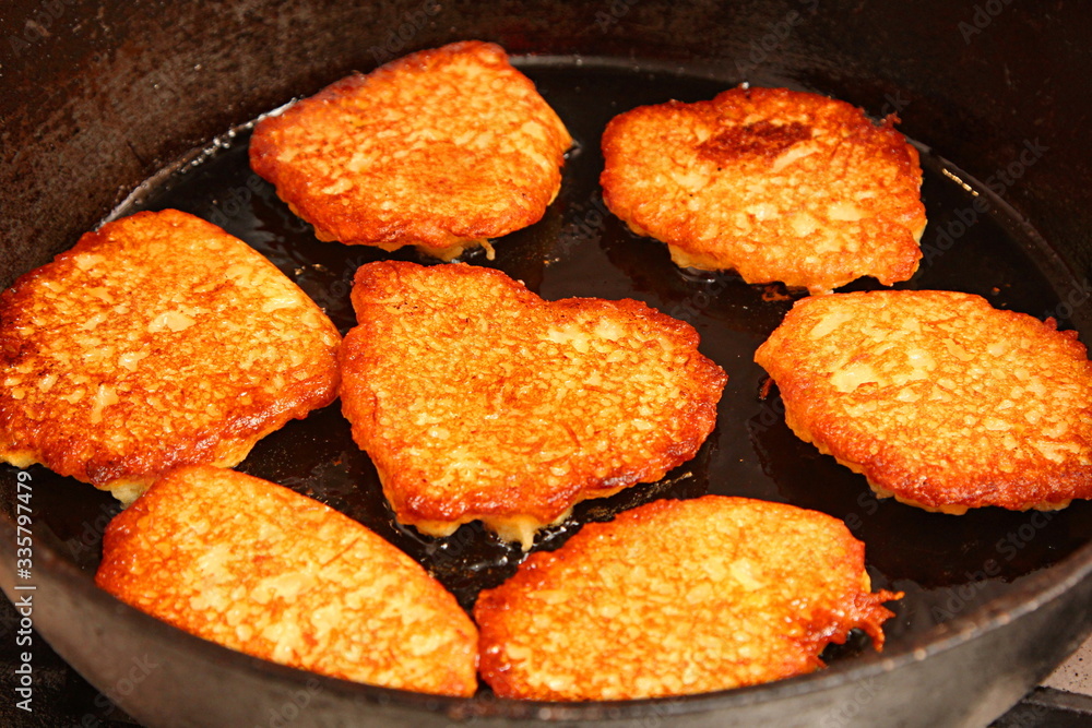 Potato pancakes fried in hot oil on black metal frying pan