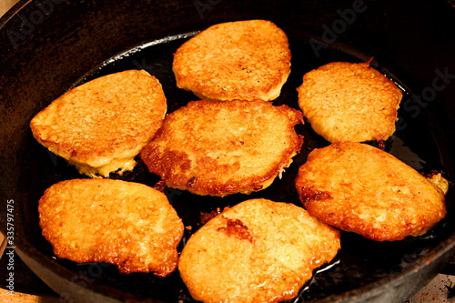 Potato pancakes fried in hot oil on black metal frying pan