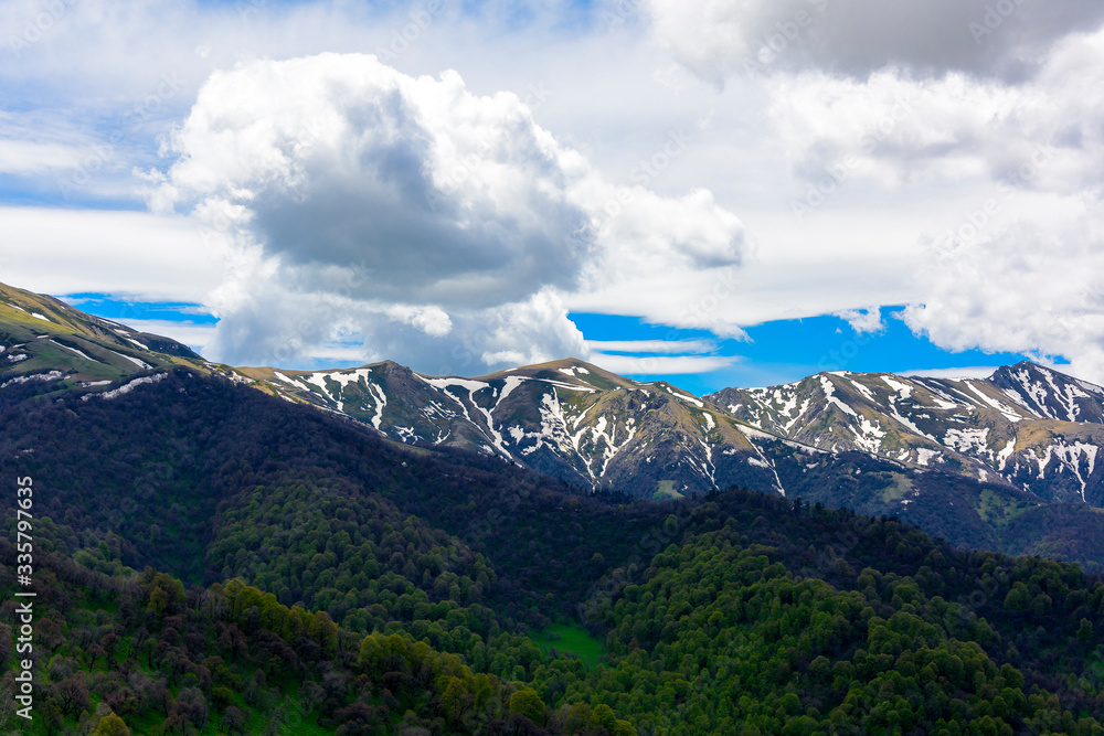 Obraz premium Beautiful mountain panorama with lush greens, blue skies, and puffy clouds