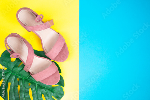Women's pink summer sandals on a yellow and blue background. Green leaf monstera. Fashionable shoes for young girls. Top view.