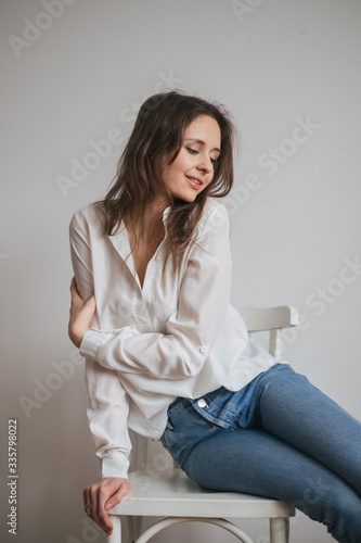 young brunette girl with long hair in a white shirt and jeans. Looks at the camera, portrait. Sexy attractive woman.