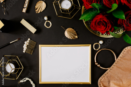 Golden blank frame with luxury golden accessories for women's beauty. Dating concept with red lipstick, roses, golden chain, earrings and handbag on black background. Elegant modern template for