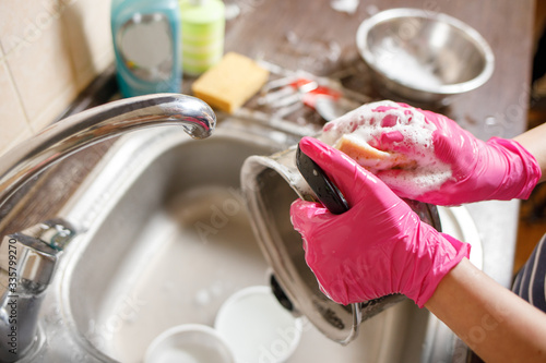 Woman in rubber gloves washing up dishes and pot