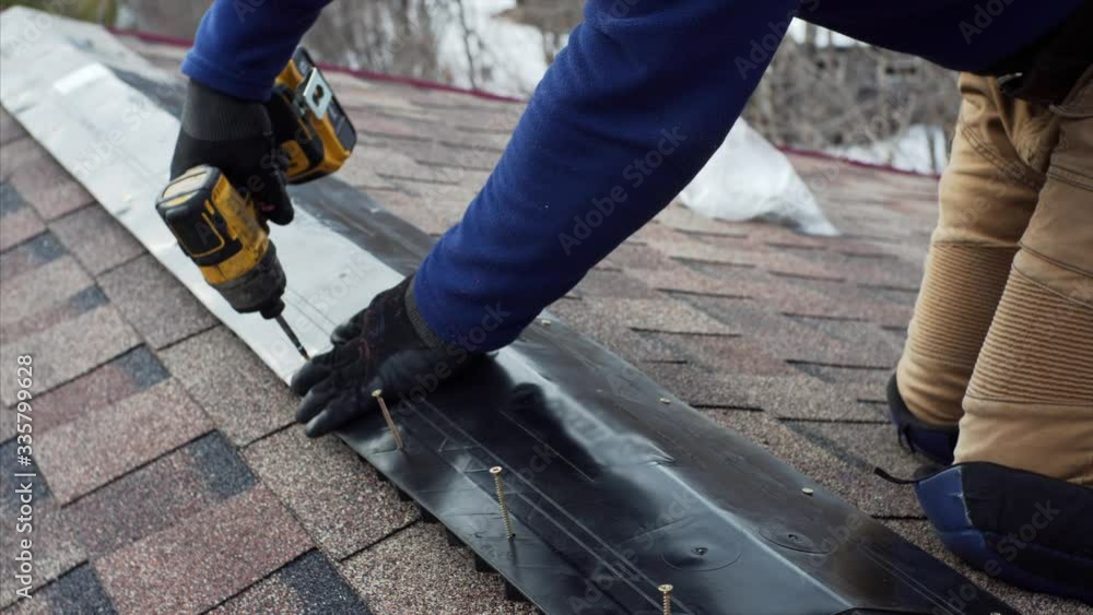 Builder is attaching ridge on the roof using a screw gun. Frame house under construction Builder is attaching ridge on the roof using a screw gun. Frame house under construction