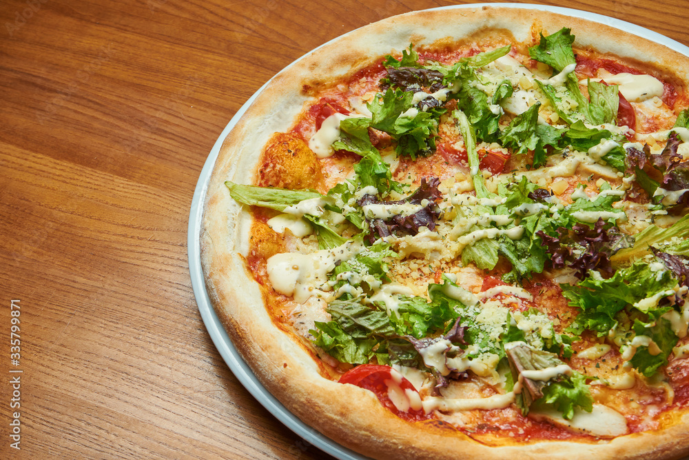 Appetizing baked Italian pizza with cream sauce, lettuce, chicken and parmesan on a white plate on a wooden background. Pizza caesar