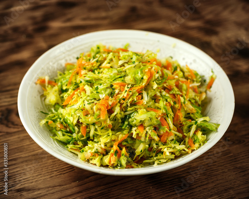 green sweet spring cabbage salad with carrots and parsley in a white bowl