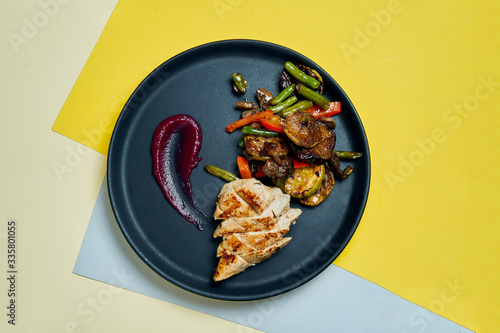 Healthy, dietary food - grilled chicken fillet with grilled vegatebles in a black ceramic plate on colored background. Close up photo