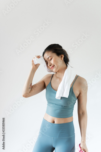A young Asian woman wipes sweat with a towel in front of a pure white background © 浩然 张