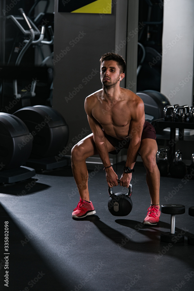 Slim muscular man lifting weights in the gym