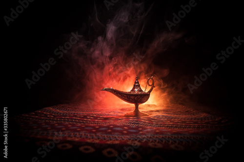Lamp of wishes concept. Antique Aladdin arabian nights genie style oil lamp with soft light white smoke, Dark background.