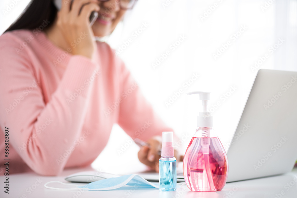 Business woman hand using smartphone with work from home. Laptop mouse, sanitizer gel, face mask, and alcohol spray for prevention Coronavirus disease (COVID-19). Healthcare disinfection concept. Business woman hand using smartphone with work from home. Laptop mouse, sanitizer gel, face mask, and alcohol spray for prevention Coronavirus disease (COVID-19). Healthcare disinfection concept.