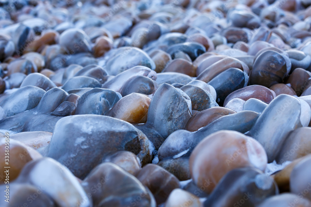 Obraz premium Colorful pebbles stone covered with ice on the shore