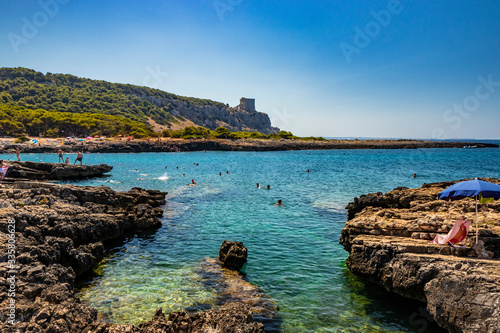 The wonderful bay of Porto Selvaggio, with pebbly and rocky beach. In Nardò, Italy, Puglia, Salento. People sunbathe and swim in the turquoise sea. The Torre dell'Alto on the promontory. Wild nature. photo