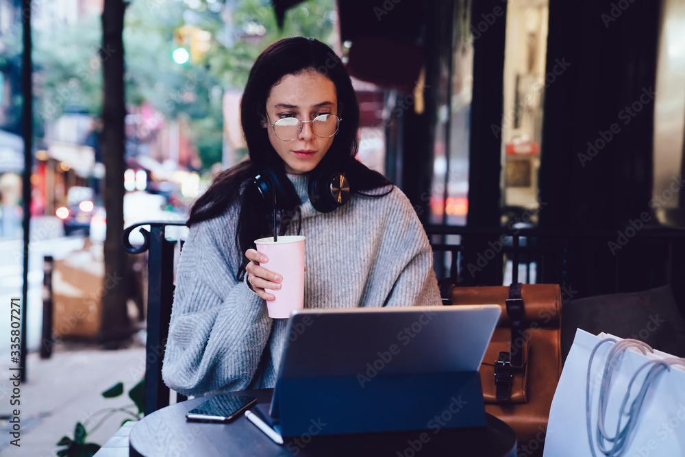 Attractive freelance woman having drink while browsing tablet in street cafe Attractive freelance woman having drink while browsing tablet in street cafe