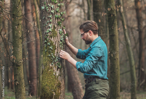 Half-length shot of curious man studying ivy twined round tree standing in bare deciduous woods