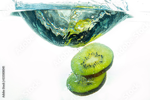 whole kiwi and sliced slices falling under water