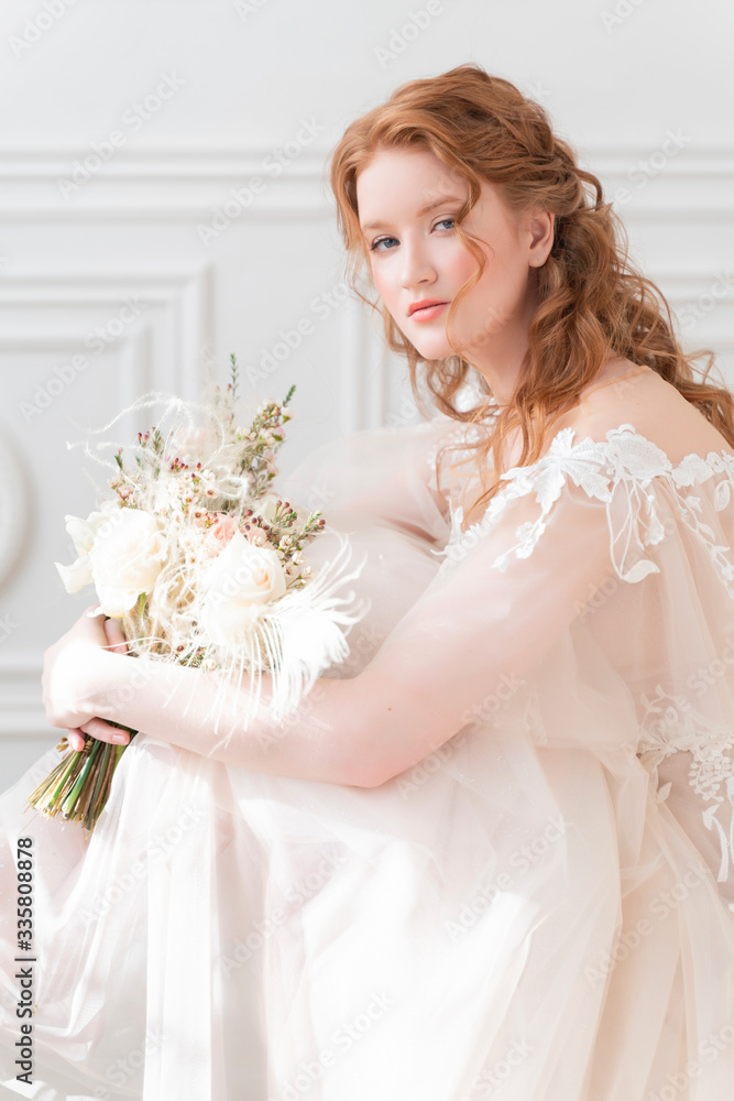 Beautiful natural redhead girl bride, with nude makeup, wearing a white dress, holds a wedding bouquet in her hands and sits on at the chair in a light interior. Beautiful natural redhead girl bride, with nude makeup, wearing a white dress, holds a wedding bouquet in her hands and sits on at the chair in a light interior.