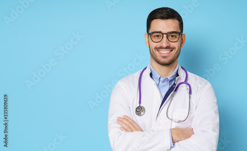 Banner of smiling young male doctor wearing white coat and round eyeglasses, isolated on blue background