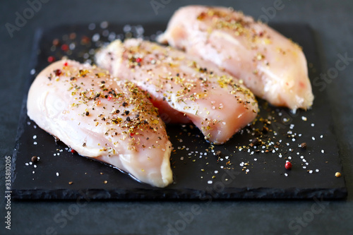 Selective focus. Raw chicken breasts with spices and sea salt on a stone board. Fresh chicken fillet marinated with herbs. Macro.