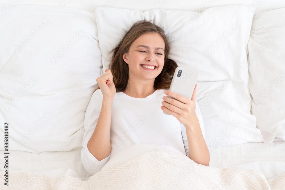 Young female smiling and laughing because after awaking in morning she saw good news about winning lottery or another success Young female smiling and laughing because after awaking in morning she saw good news about winning lottery or another success