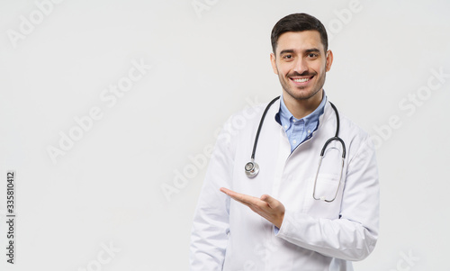 Horizontal banner of smiling young male doctor showing and presenting something with hand, isolated on gray background with copy space on the left side