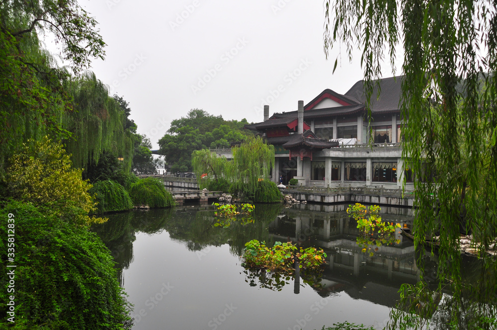 A Chinese building on the shores of West Lake in Hangzhou. The trees and the house are reflected in the water.