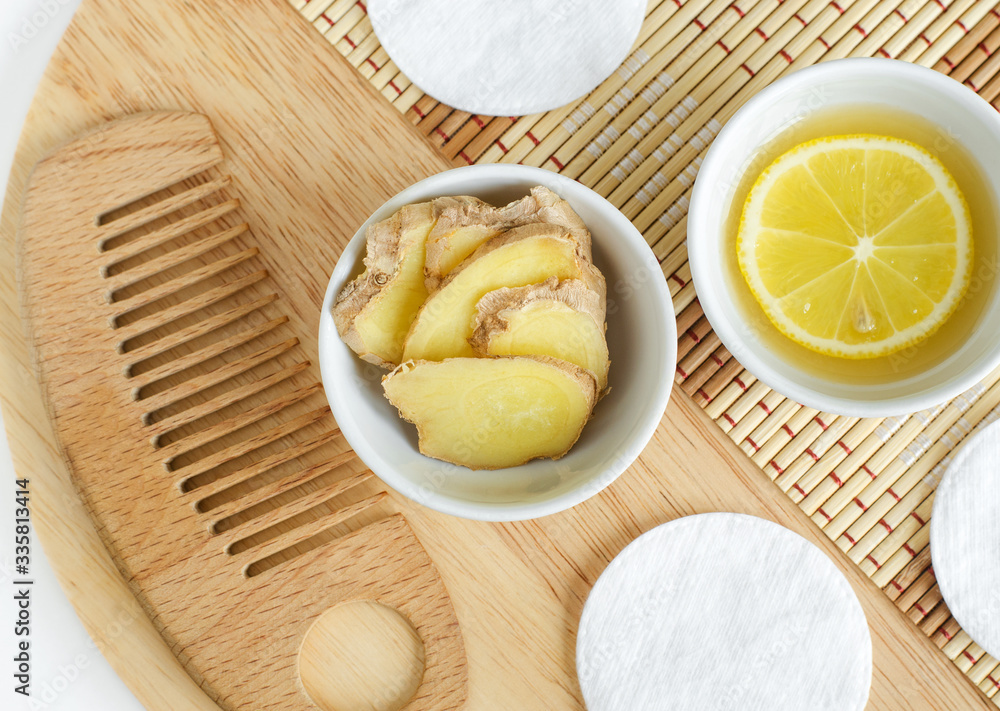 Ginger slices in the small white bowl, wooden hair comb and lemon juice and slice. Natural homemade hair treatment and zero waste concept. Top view, copy space Ginger slices in the small white bowl, wooden hair comb and lemon juice and slice. Natural homemade hair treatment and zero waste concept. Top view, copy space