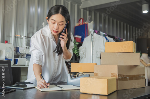 Young business woman working online e-commerce shopping at her shop. Young woman seller prepare parcel box of product for deliver to customer. Online selling, e-commerce.