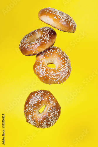 Several bagels in motion fall on a yellow background, a creative image