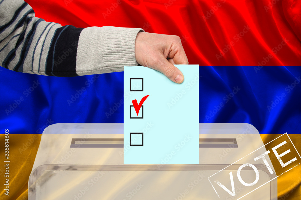 male voter drops a ballot in a transparent ballot box against the background of the national flag of Armenia, concept of state elections, referendum male voter drops a ballot in a transparent ballot box against the background of the national flag of Armenia, concept of state elections, referendum